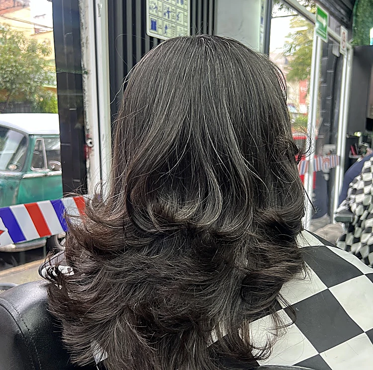 Cabello largo cortado en capas con ondas, visto de espaldas en un sillón con capa a cuadros